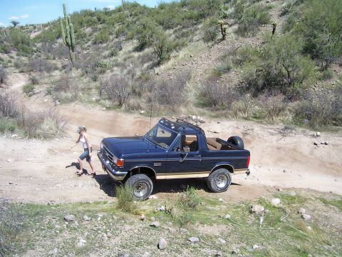1991 Ford Bronco - A 1991 Ford Bronco navigates a dusty trail in a dry, hilly environment with sparse vegetation.