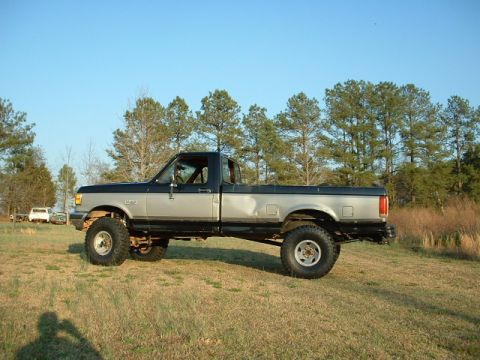 1987 Ford F-150 - Side view of a lifted 1987 Ford F-150 pickup truck with two-tone paint and large off-road tires.