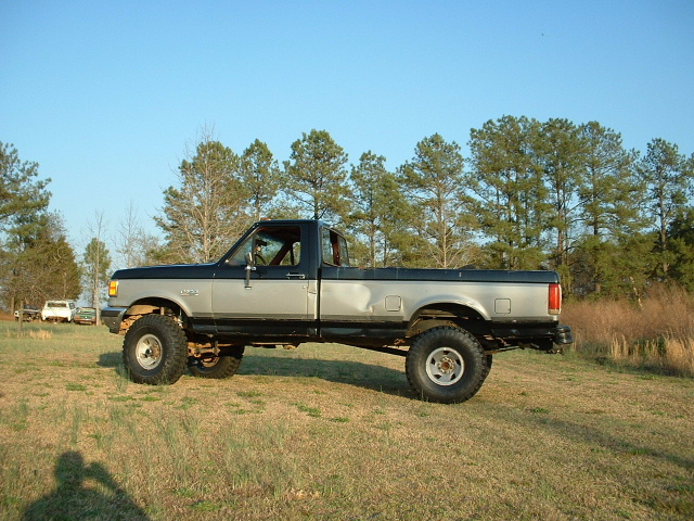 1987 Ford F-150 pickup truck, lifted with large tires, two-tone paint, parked in a grassy field
