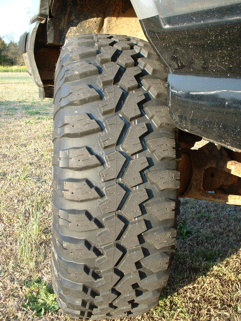 1987 Ford F-150 - A close-up view of a vehicle's tire and suspension system, with a grassy field in the background.