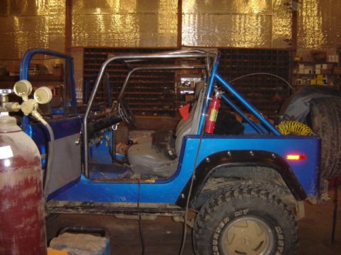 1992 Ford Bronco - A blue Jeep CJ is parked inside a workshop, possibly undergoing modifications or repairs.