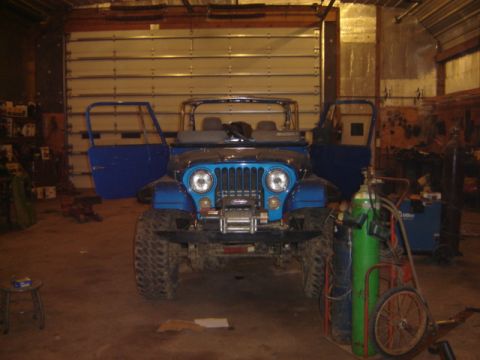 1992 Ford Bronco - A blue Jeep CJ is parked inside a garage with its doors off and a winch mounted on the front.