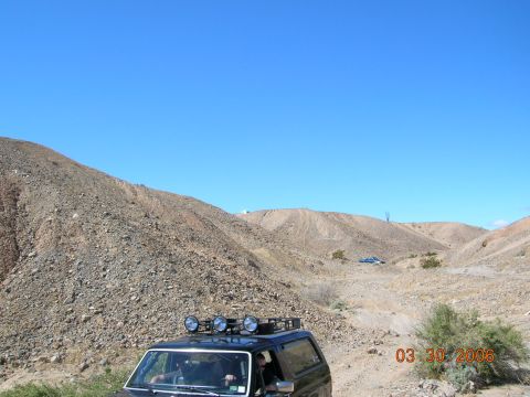 1985 Ford Bronco - A black SUV navigates a rocky desert terrain under a clear blue sky.