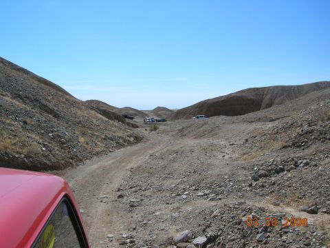1985 Ford Bronco - A view from inside a red vehicle shows a dusty, off-road canyon with multiple SUVs parked in the distance under a clear blue sky.
