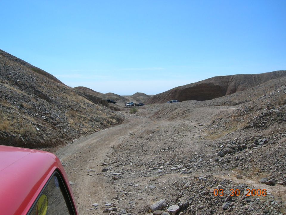 Red vehicle interior looking out at a dusty canyon with several SUVs parked in the distance