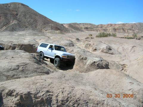 1985 Ford Bronco - A white Ford Bronco tackles a challenging off-road course in a desert landscape.