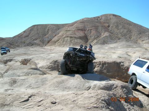 1985 Ford Bronco - Multiple off-road vehicles traversing a challenging desert terrain under a clear blue sky.