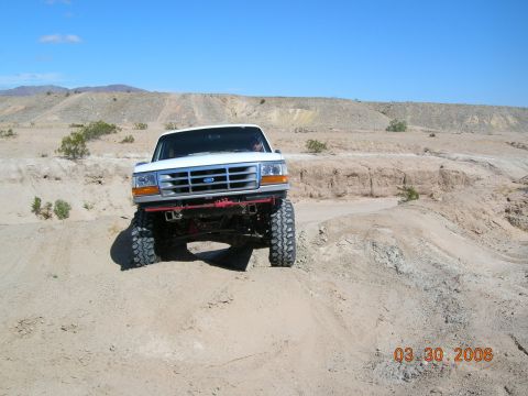 1985 Ford Bronco - This lifted white Ford Bronco is navigating a sandy off-road trail.