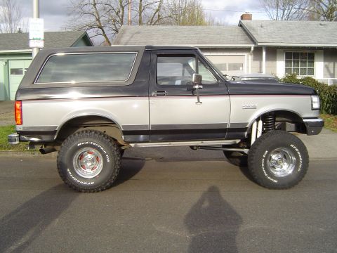 1989 Ford Bronco - This lifted 1989 Ford Bronco features a two-tone paint scheme and BFGoodrich Mud-Terrain tires, viewed from the side.