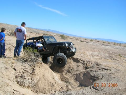 1985 Ford Bronco - A black Jeep Wrangler tackles a challenging off-road trail on a sunny day.