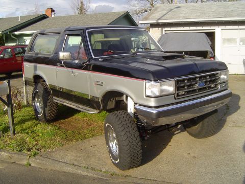 1989 Ford Bronco - This lifted 1989 Ford Bronco features a two-tone paint scheme with chrome accents and a prominent hood scoop.