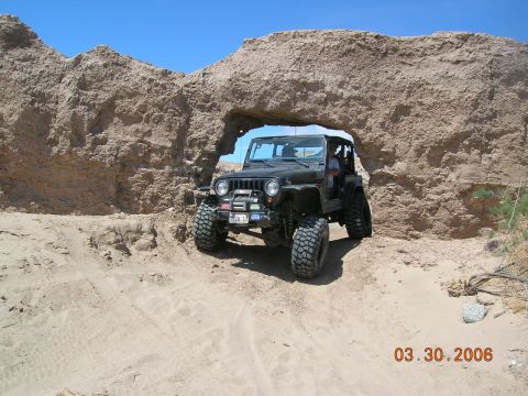 1985 Ford Bronco - Jeep Wrangler navigates a rocky archway on a sunny day.