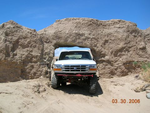 1985 Ford Bronco - A white Ford truck navigates through a natural rock formation on a sandy terrain.