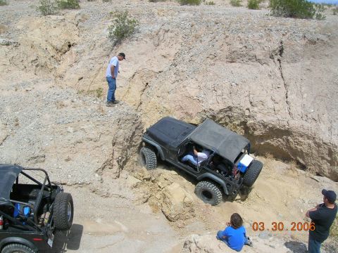 1985 Ford Bronco - People watch as Jeeps tackle a challenging off-road trail in a desert-like environment.