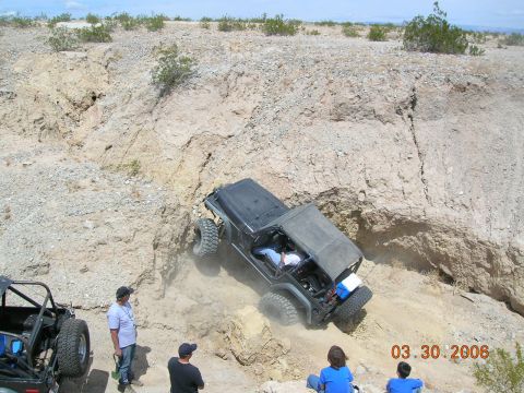 1985 Ford Bronco - Two off-road vehicles navigate a steep, rocky incline in a desert landscape.