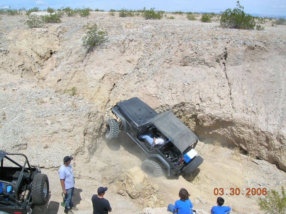 Black Jeep Wrangler climbing a dirt hill with large tires, soft top removed