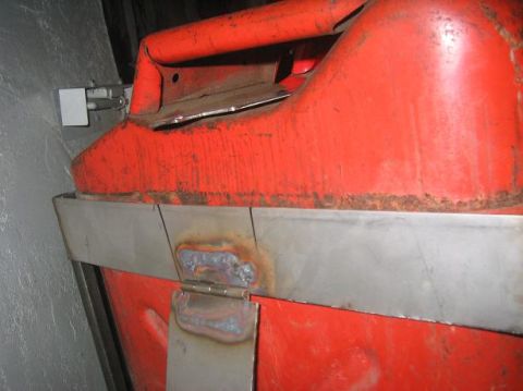 1986 Ford Bronco - Close-up of a red jerry can showing a custom metal bracket and hinge attachment, likely for a rack system.