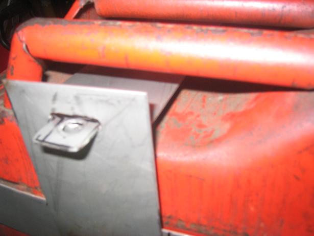Close-up of a metal bracket with a bolt hole, attached to red painted tubing