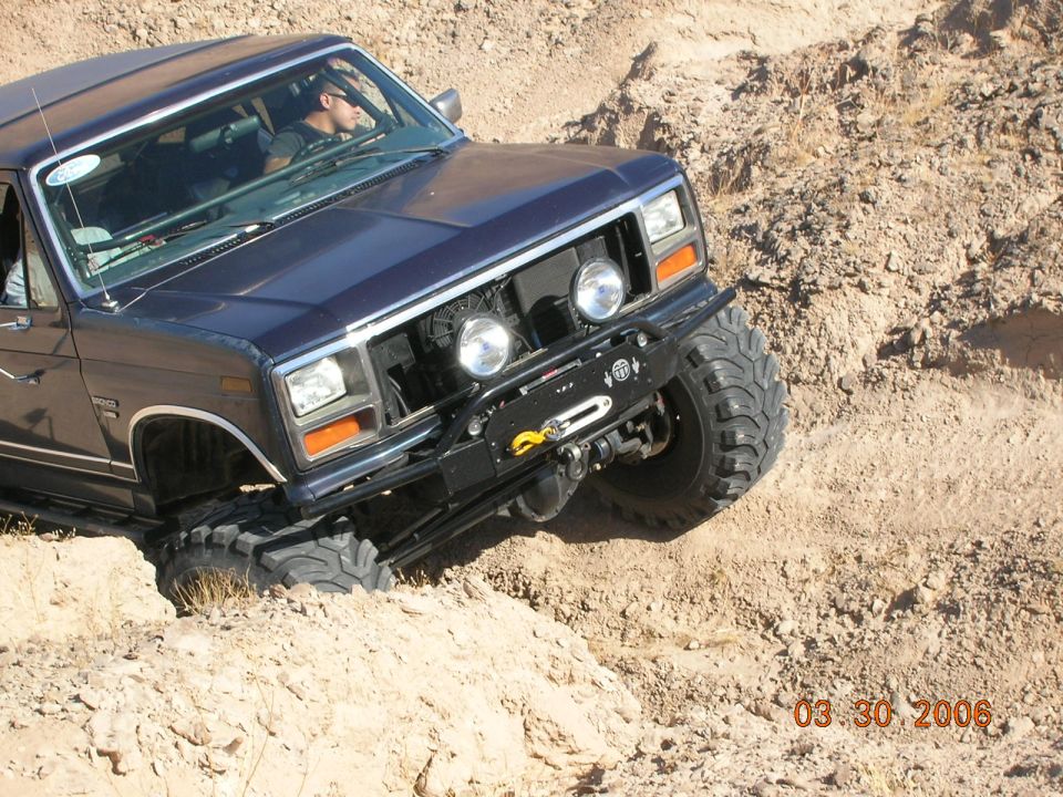 Dark blue Ford Bronco off-roading on a dirt hill, front 3/4 view