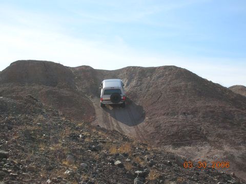 1985 Ford Bronco - A silver SUV navigates a steep dirt incline under a clear blue sky.