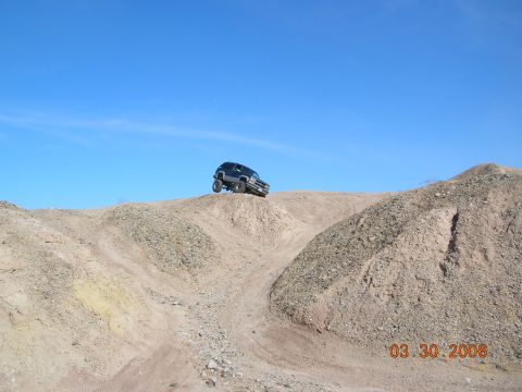 1985 Ford Bronco - SUV navigating a steep dirt incline on a sunny day.