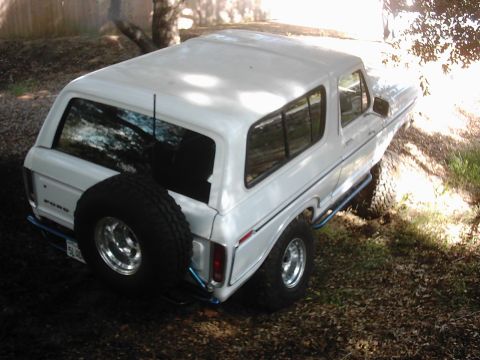 1978 Ford Bronco - This white Ford Bronco is parked outdoors on a dirt path surrounded by trees and foliage.