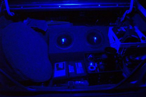 1985 Ford LTD Crown Victoria - The trunk of a car is illuminated with blue lights, showing subwoofers and audio equipment.