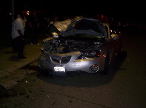 1989 Ford Bronco - A severely damaged silver Pontiac Grand Prix sits on the side of the road at night, its hood open, revealing the engine compartment.