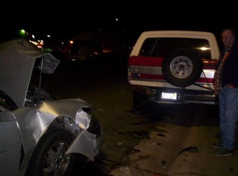 1989 Ford Bronco - A silver car with a crumpled front end sits near the rear of a red and white SUV, both appearing to have been in an accident.