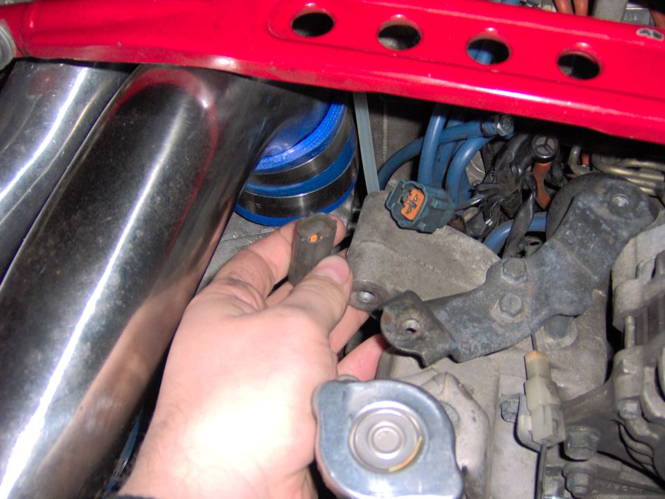 Hand holding engine part near intake manifold and red strut bar