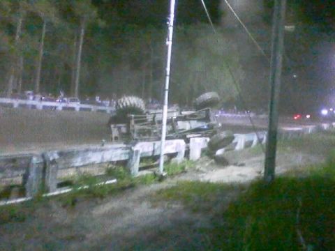 1989 Ford Bronco - A vehicle has overturned on a dirt track at night, with spectators visible in the background.
