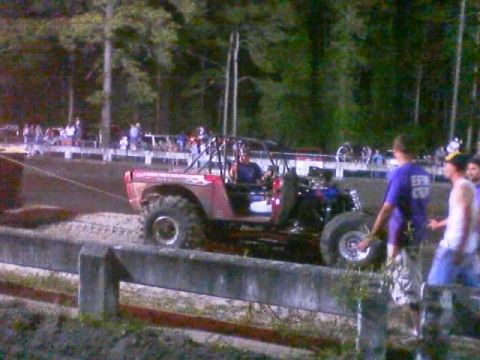 1989 Ford Bronco - A modified off-road vehicle with oversized tires navigates a dirt track, with spectators in the background.