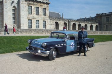 1991 Ford Crown Victoria - A uniformed officer stands next to a two-tone blue police car with 'POLICE' written on the side.