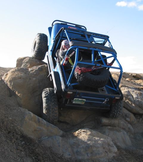 1981 Ford Bronco - A blue Jeep navigates a challenging rocky terrain, with its rear tire high off the ground.