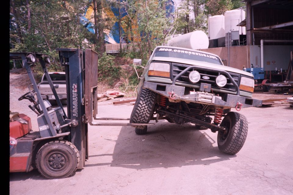 Green Ford Bronco lifted by a Toyota forklift, exposing lift kit and winch