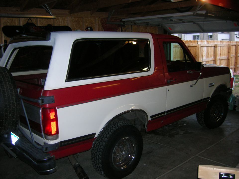 Red and white Ford Bronco parked in a garage, rear-mounted spare tire visible