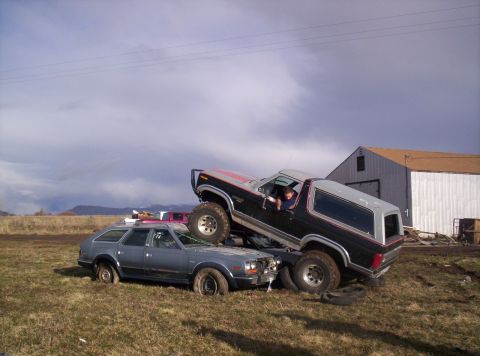 1984 Ford Bronco - A Ford Bronco is crushing a station wagon in a grassy field.