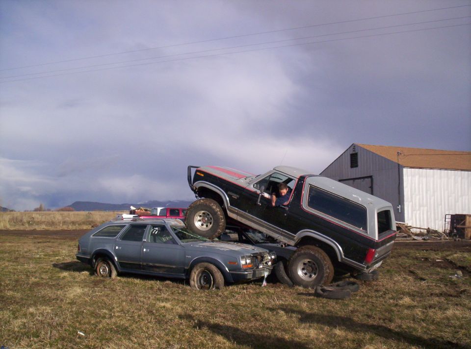 Ford Bronco on top of a station wagon in a field with a barn in the background