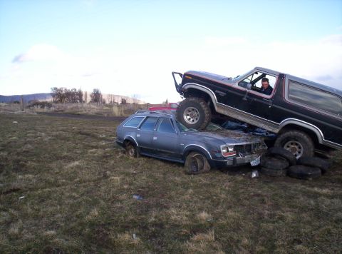 1984 Ford Bronco - A Ford Bronco is parked on top of an AMC station wagon in a field.