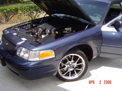1998 Ford Crown Victoria - A dark blue Ford Crown Victoria sedan photographed from the front-left three-quarter angle with its hood open, exposing the V8 engine bay.…