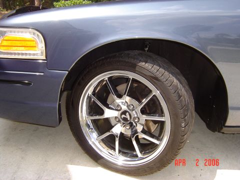 1998 Ford Crown Victoria - Close-up of the front fender and chrome wheel on a blue 1998 Ford Crown Victoria.