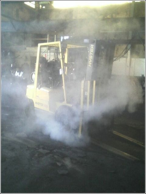 1979 Ford Bronco - A yellow forklift is seen emitting a large cloud of white smoke from its side in an industrial setting.