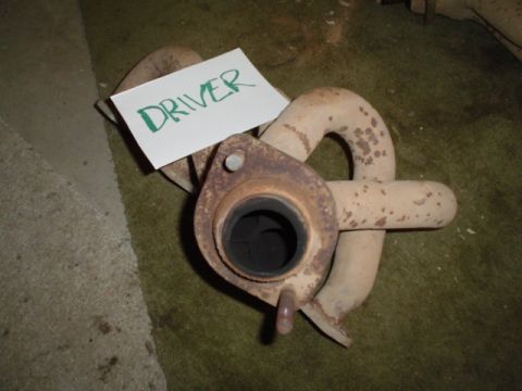 1981 Ford Bronco - Cast-iron exhaust manifold resting on green carpet with a hand-lettered DRIVER sign propped against it, shot looking straight down the coll…