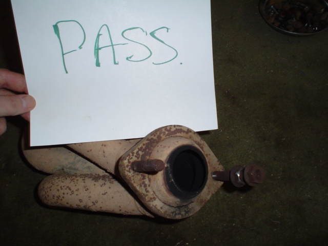 Exhaust manifold collector outlet with rusty studs, labeled PASS on a paper sign