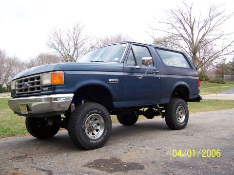 1987 Ford Bronco - A blue 1987 Ford Bronco SUV is shown from a three-quarter front angle, lifted with off-road tires.