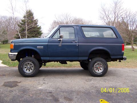 1987 Ford Bronco - This lifted blue Ford Bronco is shown from the side, equipped with off-road tires.