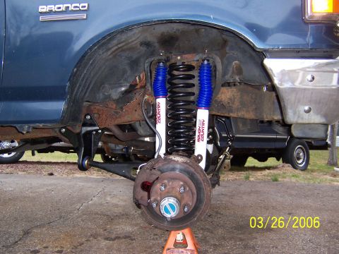 1987 Ford Bronco - The front wheel well of a blue Ford Bronco shows new suspension components and some rust on the frame.