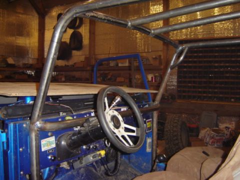 1992 Ford Bronco - The interior of a custom blue off-road vehicle is shown with a prominent roll cage and aftermarket steering wheel.