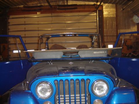 1992 Ford Bronco - The front grille and round headlights of a blue Jeep CJ are visible, with its doors open in a garage setting.