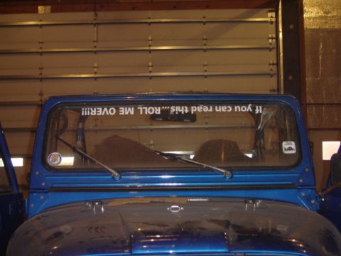 1992 Ford Bronco - A blue Jeep CJ is parked indoors, with a humorous sticker on its windshield.